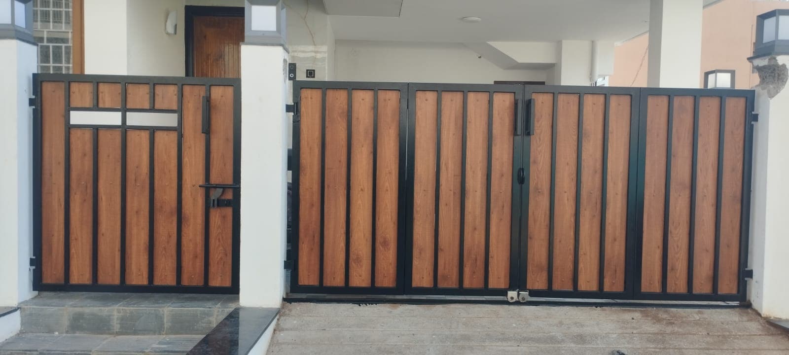 Modern bi-folding main gate with matching pedestrian entrance in wood and black metal