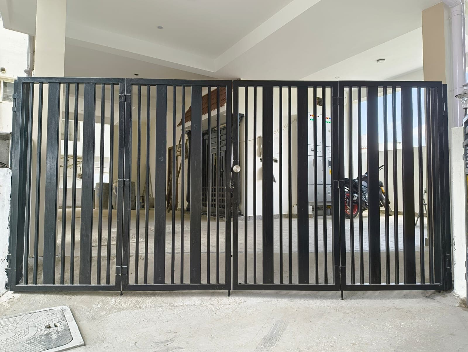 Matte black bi-folding industrial security gate with vertical slats and stainless handle